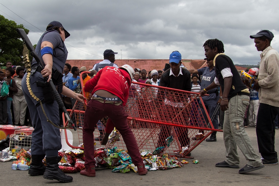 In order to avoid bloodshed the goods from a Pakistani shop are placed in the road to be dispersed amongst a crowd following an attempted break-in on Albany Road in Grahamstown on 23 October 2015. Police, security and community leaders assisted in the removal of all valuable goods before the perishables were given away. Photo: Jeff Stretton-Bell