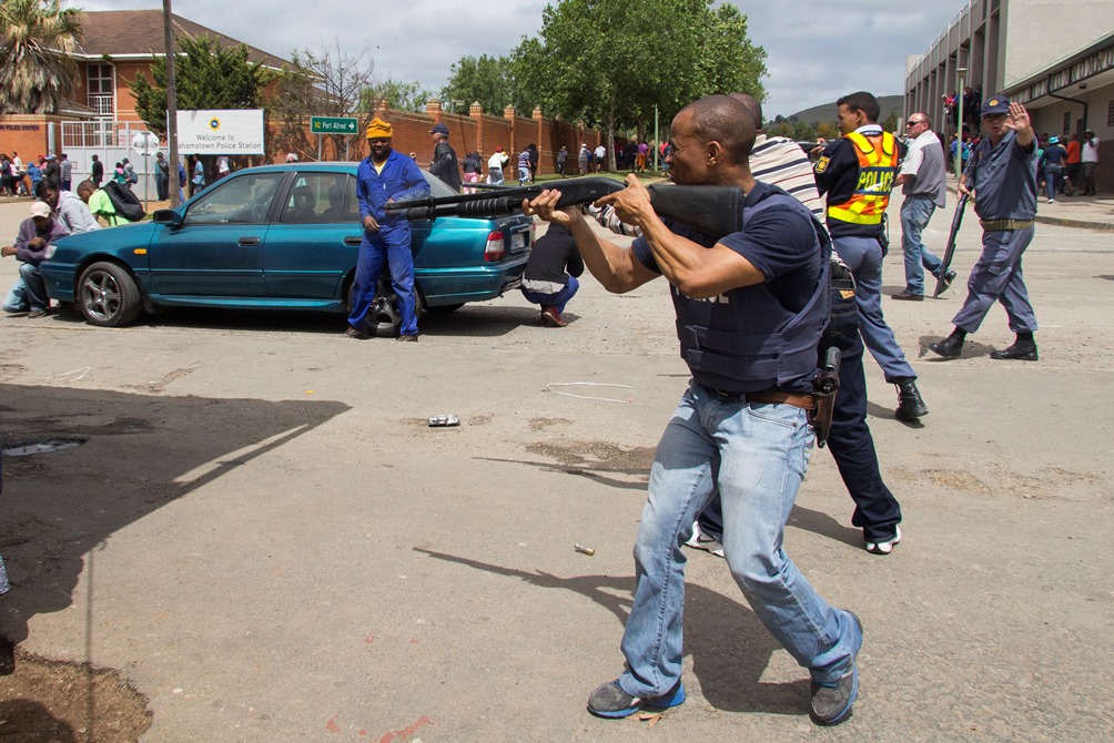 An policeman calls for fellow officers to cease firing after a crowd was dispersed with rubber bullets in Grahamstown, Eastern Cape on 22 October 2015. The town was in turmoil as residences looted shops belonging to foreign shop owners suspected for a spree of murders and corps mutilations. Photo: Jeff stretton-Bell