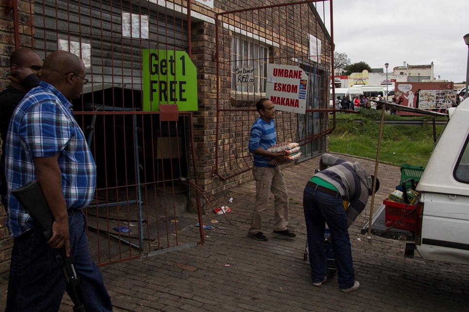 Police stand guard as shop owners clear their looted shop in Grahamstown, Eastern Cape on 22 October 2015. The town was in turmoil as residences looted shops belonging to foreign shop owners suspected for a spree of murders and corps mutilations. Photo: Jeff stretton-Bell